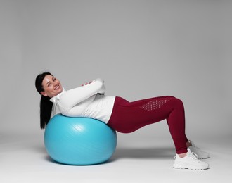 Photo of Plus size woman in gym clothes with fitness ball on grey background