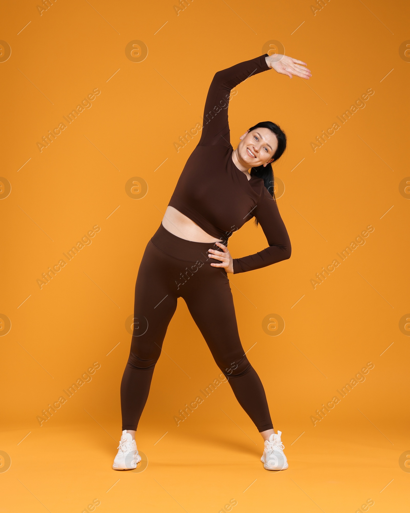 Photo of Plus size woman in gym clothes exercising on orange background