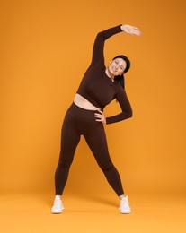 Plus size woman in gym clothes exercising on orange background