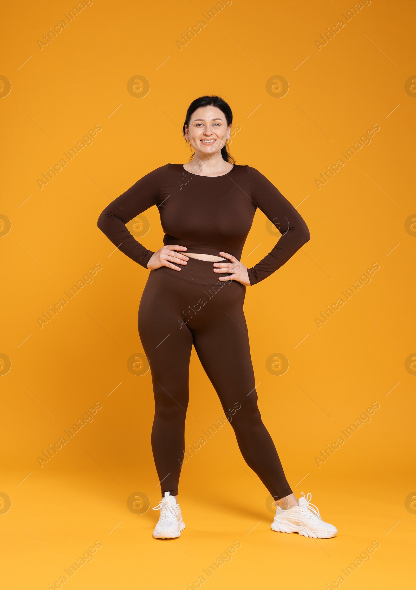 Photo of Plus size woman in gym clothes on orange background