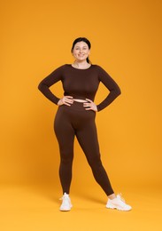 Plus size woman in gym clothes on orange background