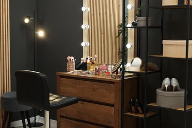 Photo of Makeup room. Wooden dresser with mirror, different beauty products, shoes and chair indoors