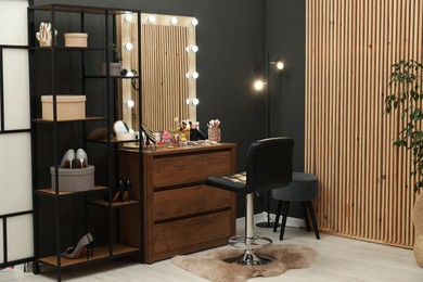 Photo of Makeup room. Wooden dresser with mirror, different beauty products, shoes and chair indoors