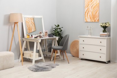 Photo of Makeup room. Mirror, dressing table, different beauty products and chair indoors