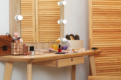 Photo of Makeup room. Mirror, wooden dressing table and different beauty products indoors