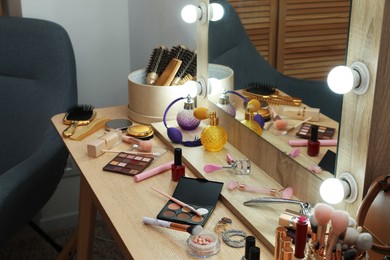 Photo of Makeup room. Mirror, wooden dressing table and different beauty products indoors