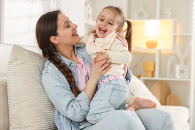 Photo of Happy mother having fun with her little daughter on sofa at home