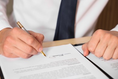 Photo of Man putting signature on document at table, closeup