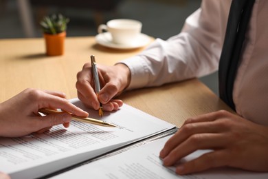 Photo of Woman pointing at document and man putting signature at wooden table, closeup