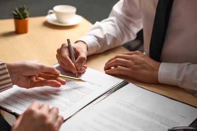 Photo of Woman pointing at document and man putting signature at wooden table, closeup