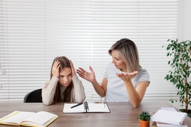 Photo of Annoyed mother and her stressful daughter doing homework at table indoors