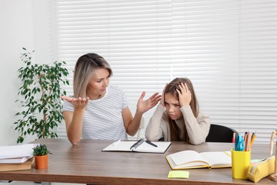 Photo of Annoyed mother and her stressful daughter doing homework at table indoors