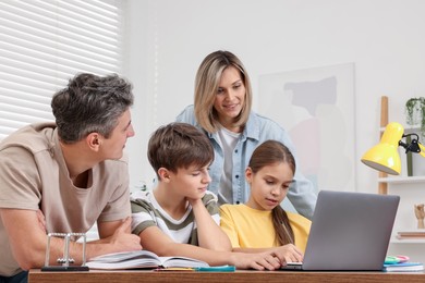 Photo of Parents and their children doing homework with laptop at table indoors