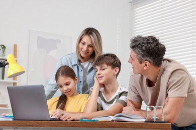 Photo of Parents and their children doing homework with laptop at table indoors