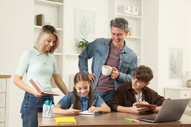 Photo of Happy parents and their children doing homework with laptop at table indoors