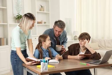 Photo of Happy parents and their children doing homework with laptop at table indoors