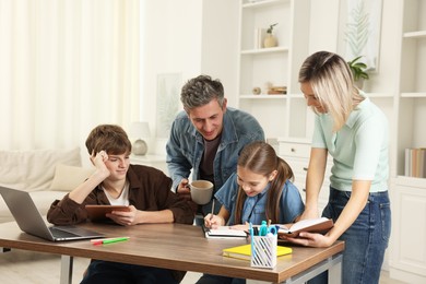 Photo of Happy parents and their children doing homework with laptop at table indoors