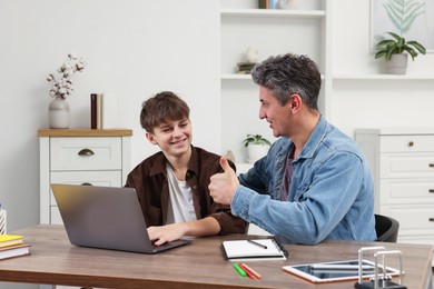 Photo of Father showing thumbs up to his son while they doing homework with laptop at table indoors