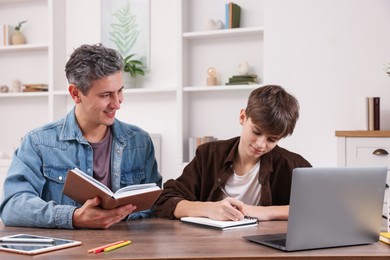 Smiling father helping his son with homework at table indoors