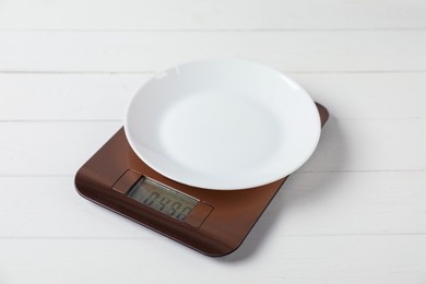 Photo of Modern electronic kitchen scale with plate on white wooden table, closeup