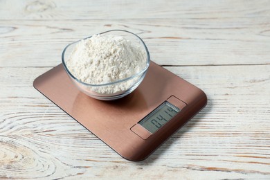 Photo of Modern electronic kitchen scale with bowl of flour on wooden table, closeup