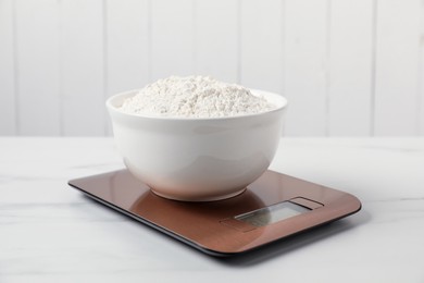 Photo of Modern electronic kitchen scale with bowl of flour on white marble table, closeup