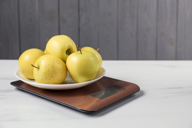 Photo of Modern electronic kitchen scale with apples on white marble table, closeup. Space for text