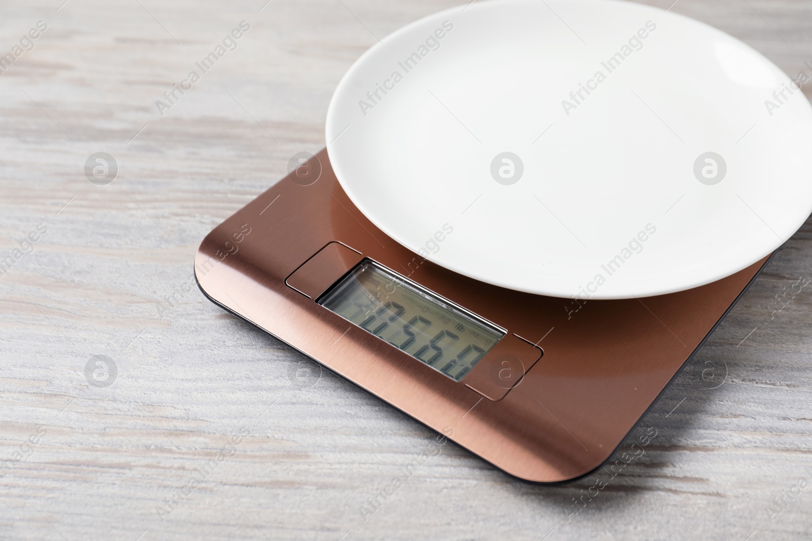 Photo of Modern electronic kitchen scale with plate on wooden table, closeup. Space for text