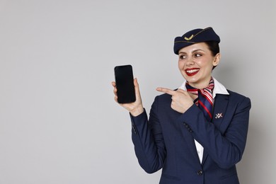 Smiling stewardess pointing at smartphone on grey background. Space for text