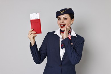 Excited stewardess holding passport with flight tickets on grey background