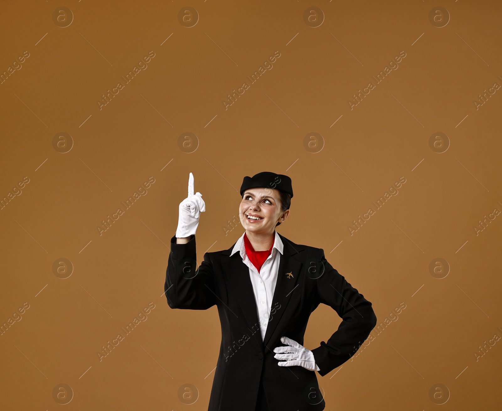 Photo of Smiling stewardess pointing upwards on brown background. Space for text