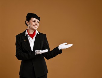 Photo of Smiling stewardess showing something on brown background. Space for text