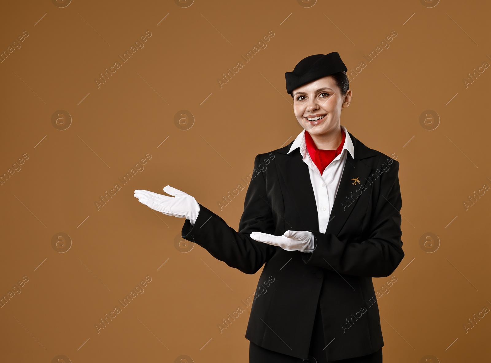 Photo of Smiling stewardess showing something on brown background. Space for text