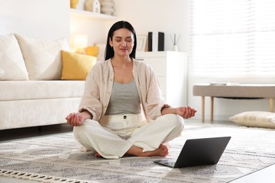 Woman with laptop meditating on floor at home