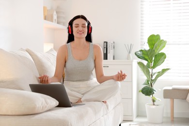 Woman with laptop meditating on sofa at home