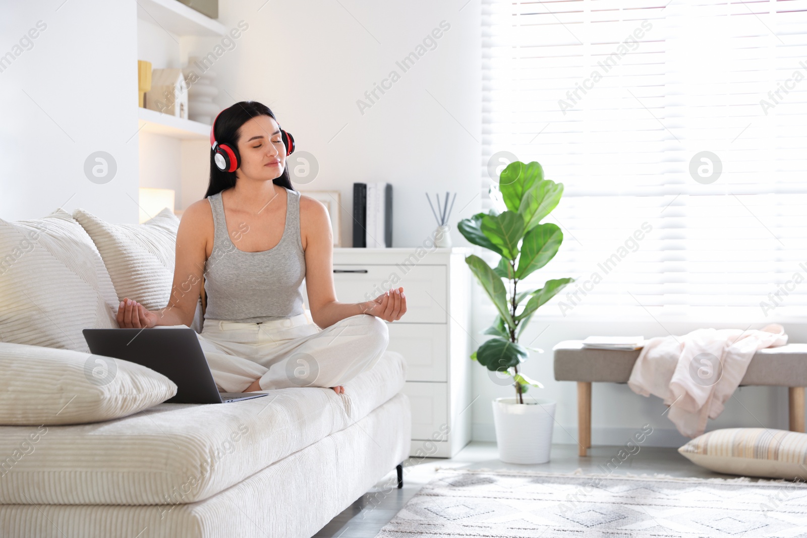 Photo of Woman with laptop meditating on sofa at home. Space for text