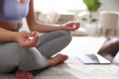 Woman with laptop meditating on floor at home, closeup