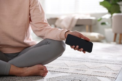 Photo of Woman with smartphone meditating on floor at home, closeup