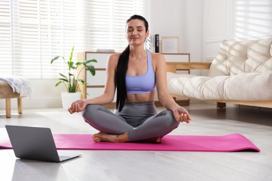 Woman with laptop meditating on floor at home