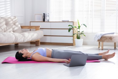 Woman with laptop meditating on floor at home