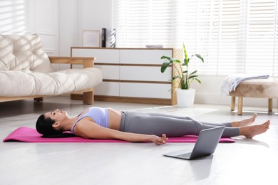 Woman with laptop meditating on floor at home