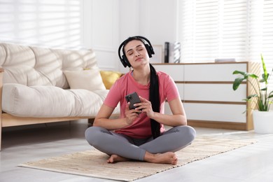 Woman with smartphone meditating on floor at home