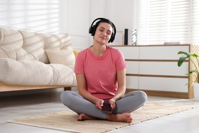 Photo of Woman with smartphone meditating on floor at home