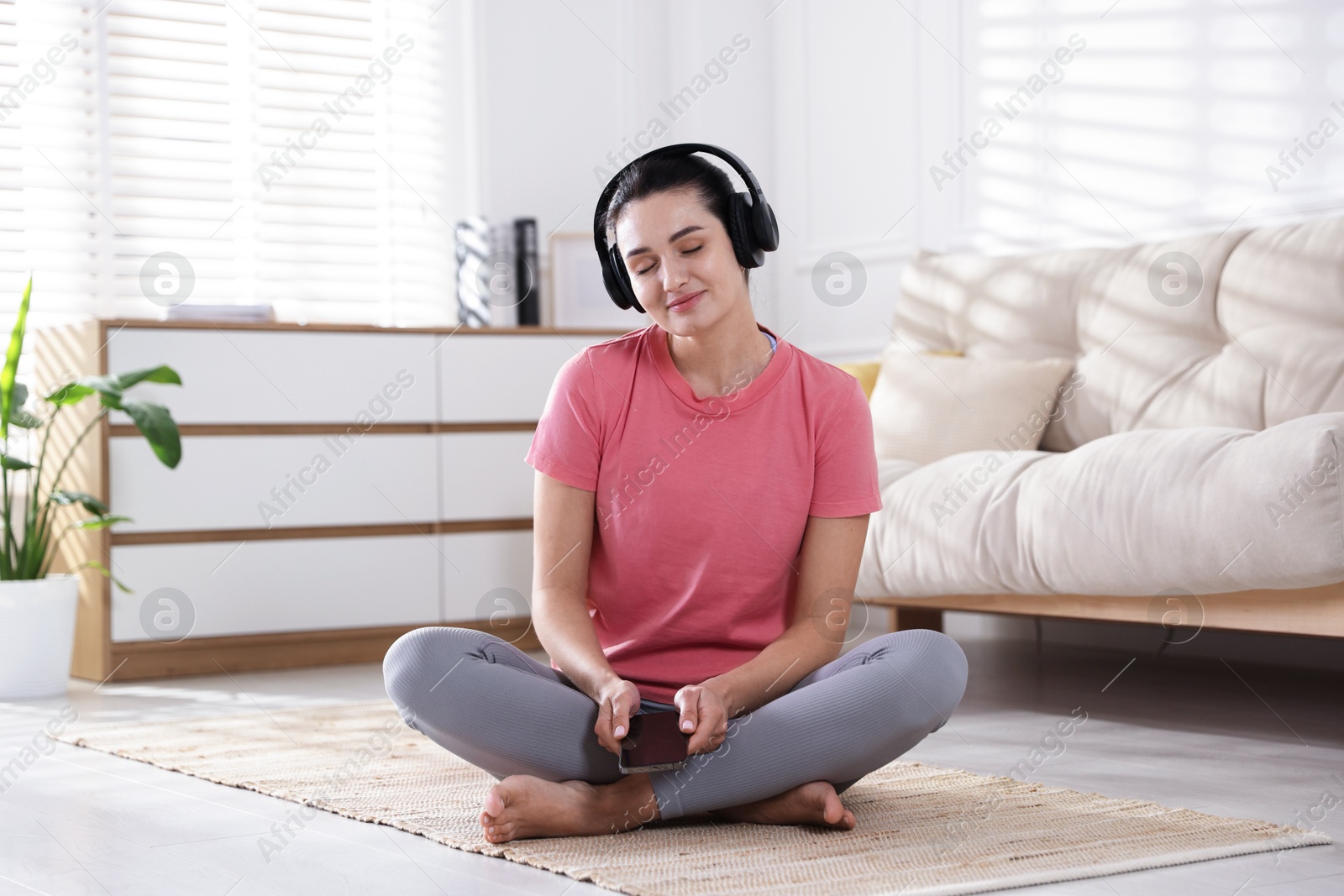 Photo of Woman with smartphone meditating on floor at home