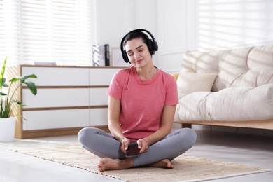 Photo of Woman with smartphone meditating on floor at home