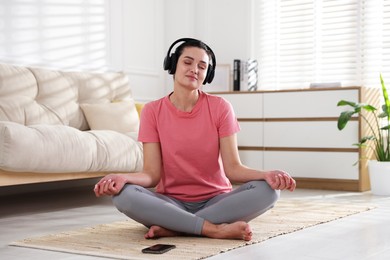 Photo of Woman with smartphone meditating on floor at home