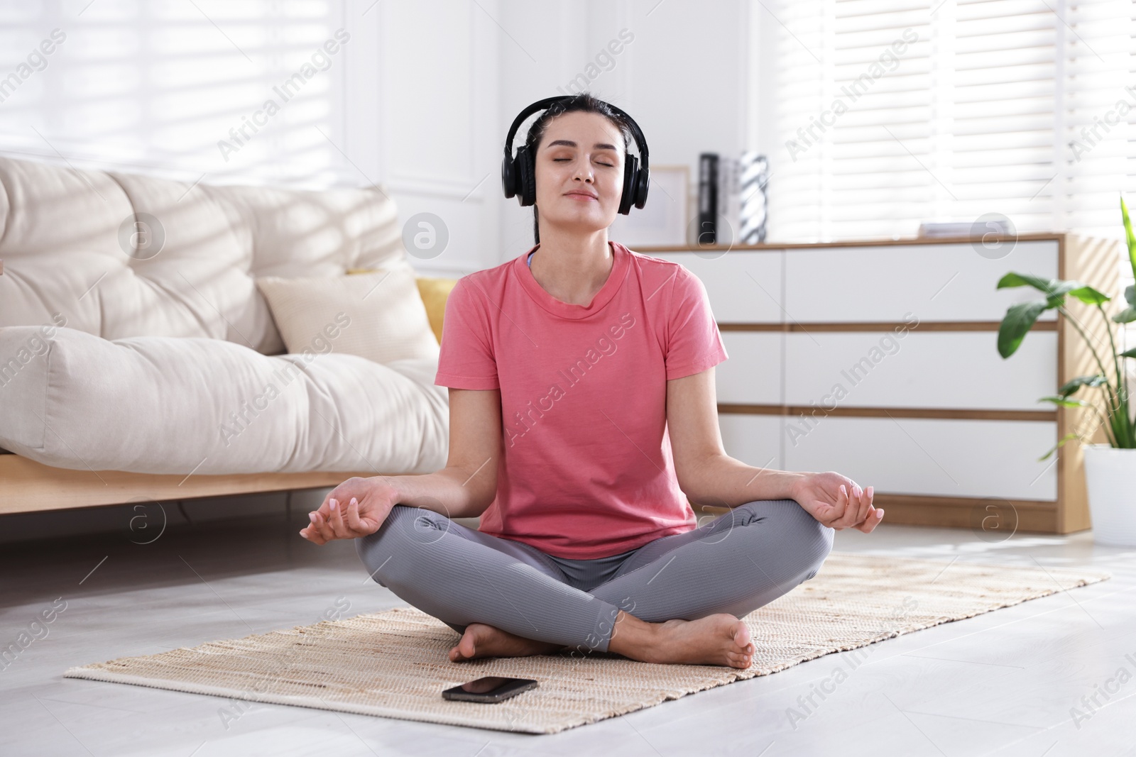 Photo of Woman with smartphone meditating on floor at home