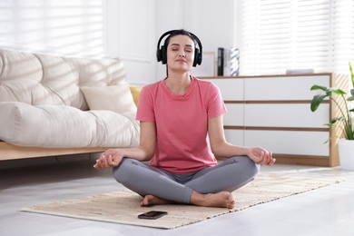 Photo of Woman with smartphone meditating on floor at home