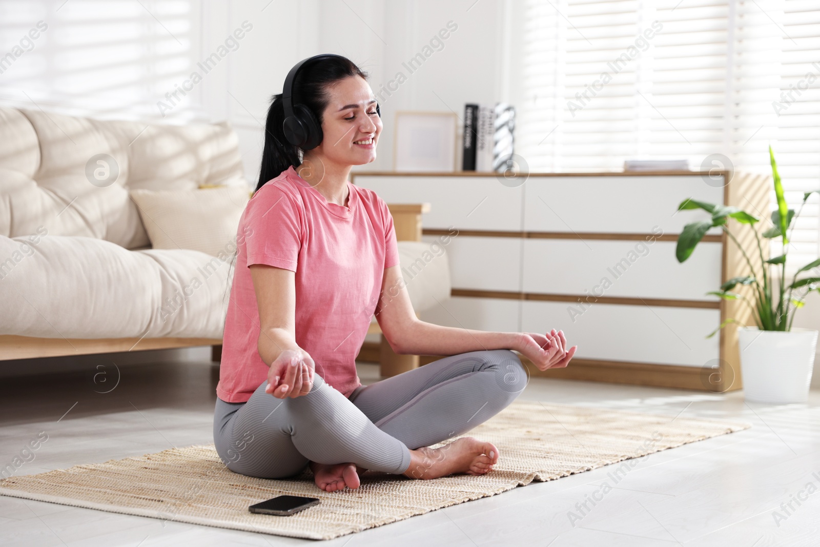 Photo of Woman with smartphone meditating on floor at home