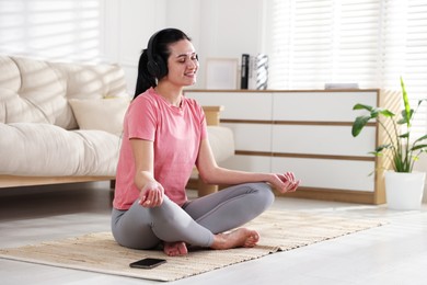 Woman with smartphone meditating on floor at home